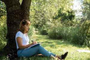 Tina writing by stream under tree